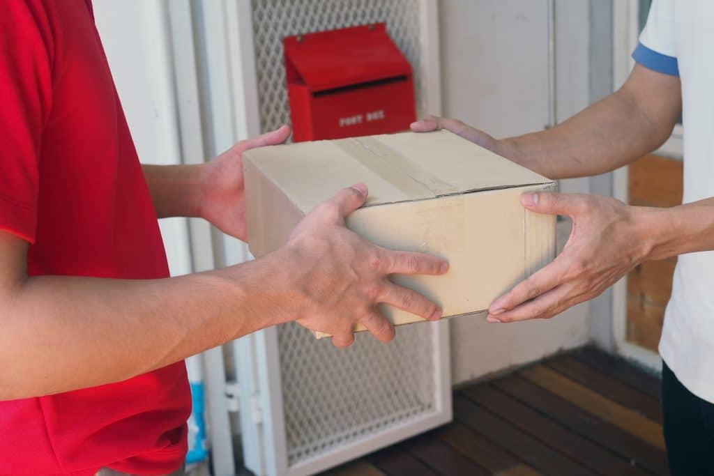 A courier wearing red handing a box to a customer. This is to represent “DPD vs Royal Mail: Which is Better for UK Shipping?”