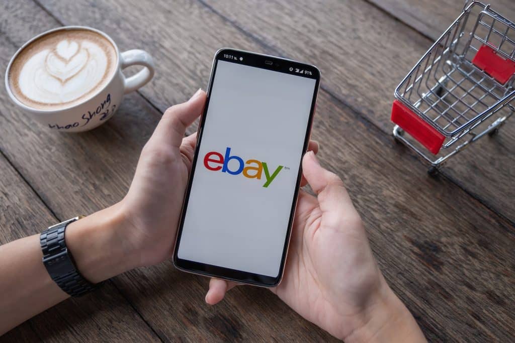 A man drinking a latte looking on his phone for the top selling items on ebay