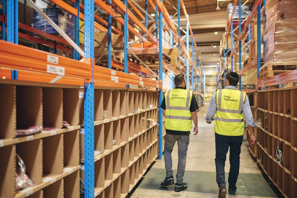 Two Delta Fulfilment colleagues walking through the warehouse to represent ‘3PL vs Amazon FBA: Which Fulfilment Model is Better?’
