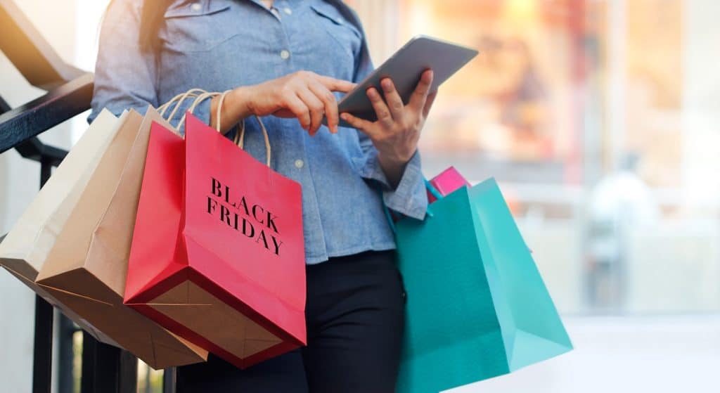 A woman online shopping on an ipad while holding shopping bags on Black Friday 2024
