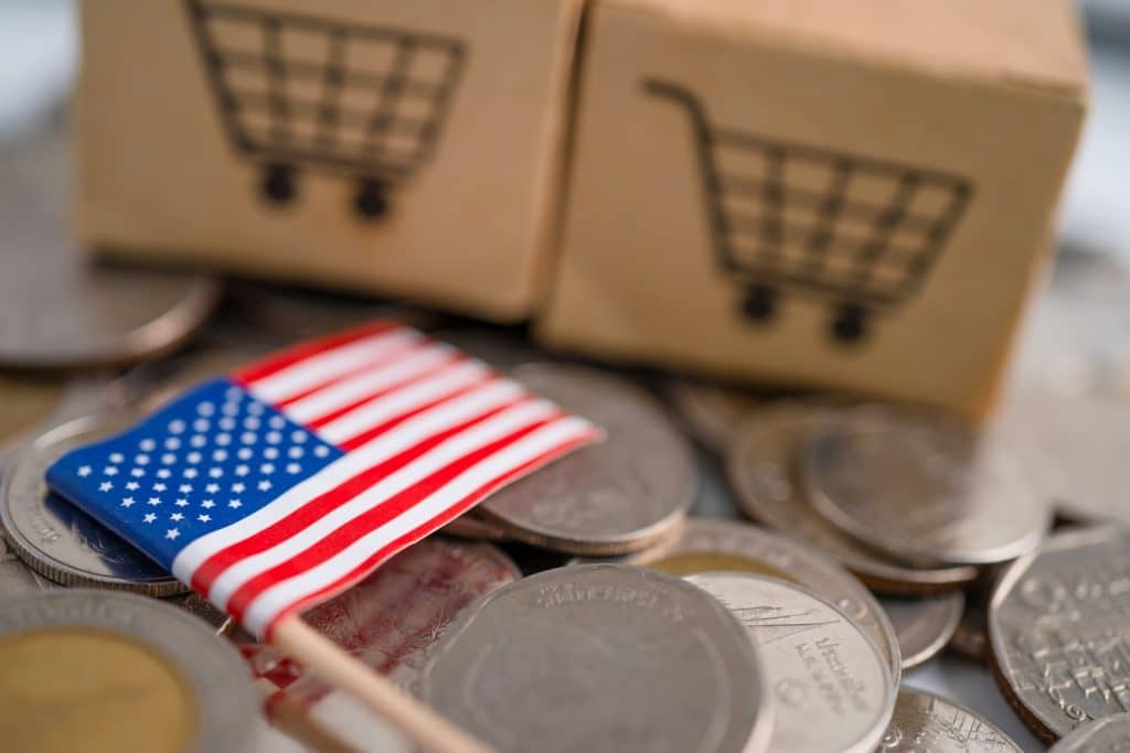 American flag on top of coins and boxes in the background, with shopping carts representing selling online to the USA